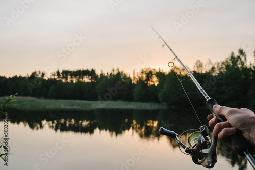 Fisherman with rod, spinning reel on the river bank. Sunrise. Fishing for pike, perch, carp. Fog against the backdrop of lake. background Misty morning. wild nature. The concept of a rural getaway.