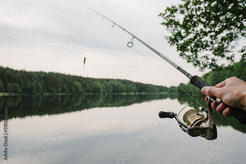 Fisherman with fishing rod, spinning reel on the background river bank. Sunrise. Fishing the backdrop of lake.