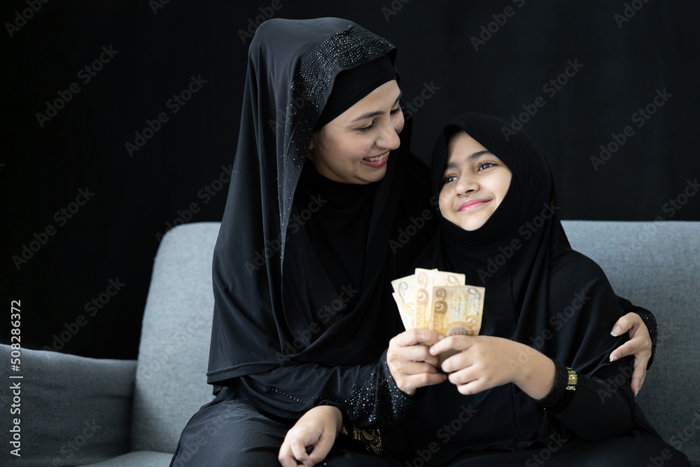 muslim woman or mother giving cash money to her daughter on black background