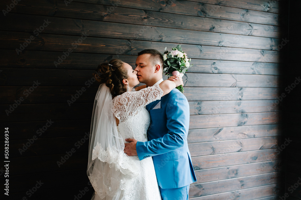The bride and groom on wooden wall background. First meeting. Newlyweds kissing indoors. Happy wedding day of marriage. The bride and groom on wooden wall background. First meeting. Newlyweds kissing indoors. Happy wedding day of marriage.