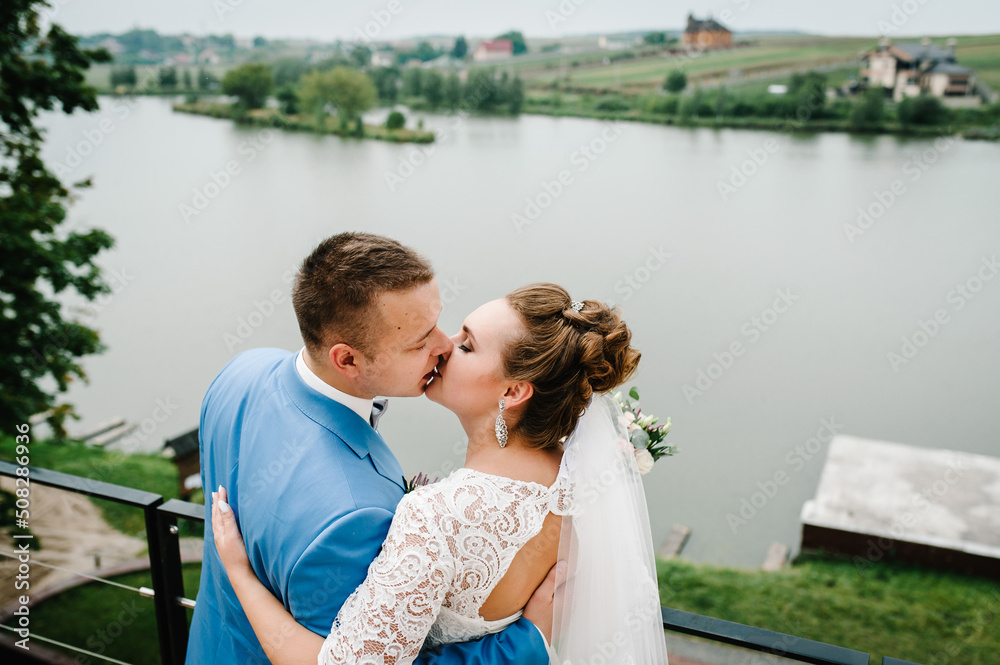 The bride and groom kiss on wedding ceremony on pier. A newlyweds couple in a country. Photo near lake outdoors. The bride and groom kiss on wedding ceremony on pier. A newlyweds couple in a country. Photo near lake outdoors.