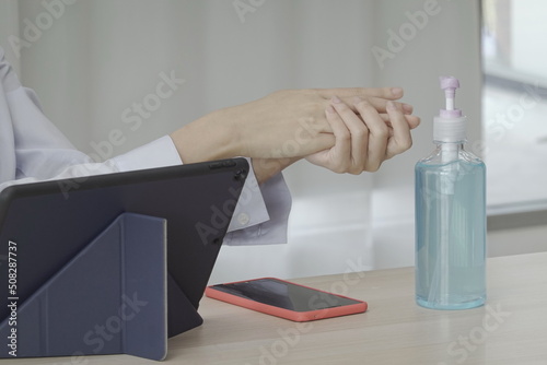 A female worker washes her hands with disinfectant alcohol gel to keep her hands clean and safe from COVID-19. Before picking up your cell phone on the table. Place a bottle of hand sanitizer on table