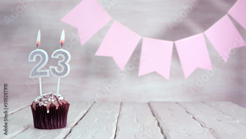Birthday number 23. Festive background for a girl or woman with a muffin and candles burning pink in pastel colors with decorations for any holiday, copy space, women's gift boxes, place for text.