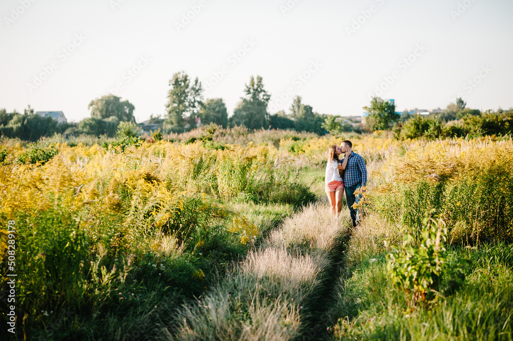 Young couple kissing on grass and hugging at sunset in spring an outdoor. A man and woman on the field on background of sun. Concept of love and family. full length. Close Up.