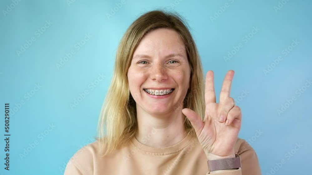 Young woman with dental braces laughing isolated on blue colour background. Studio. Cute lovely girl with metal braces on white clear teeth smiling in clinic. Close Up. Positive Emotion. Stomatology. Young woman with dental braces laughing isolated on blue colour background. Studio. Cute lovely girl with metal braces on white clear teeth smiling in clinic. Close Up. Positive Emotion. Stomatology.
