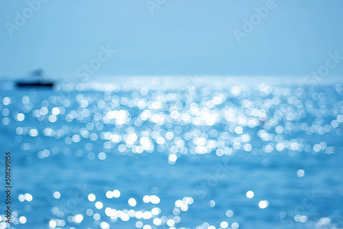 Soft focus bokeh light effects over a rippled, blue water background with lens flare and silhouette boat.