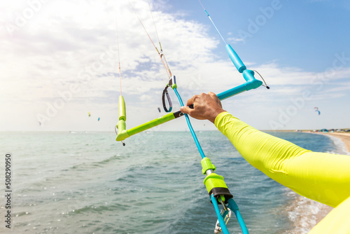 Young adult caucasian fit male person adjust kite surf board bar in sun uv protection suit on bright sunny day against blue sky at sea or ocean shore. Watersport adrenaline fun adventure acitivity photo