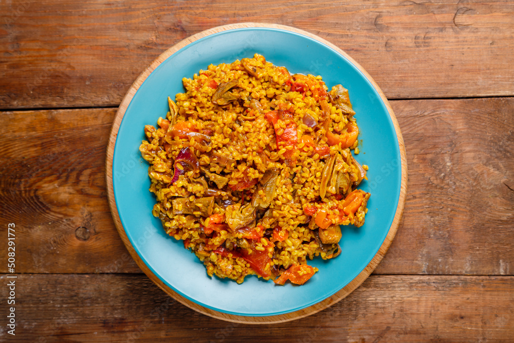 Big dish of bulgur with vegetables and mushrooms on the table.