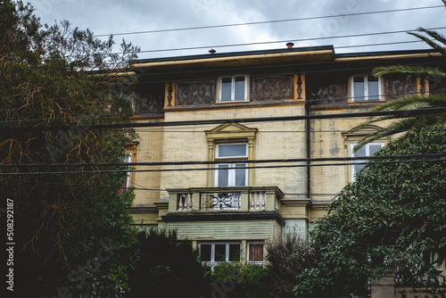 Old abandoned three story old centuries stone and bricks house with balcony, ornamentation and trees and palms in a cloudy day, Valdivia, Chile