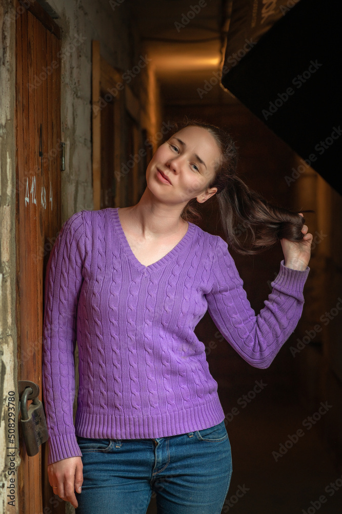 Portrait of a young beautiful girl in jeans and a blouse in a dark room.