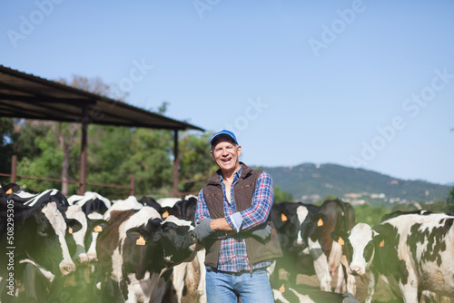 The farmer is happy next to a large herd of cows.