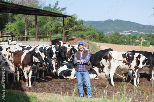 The farmer is happy next to a large herd of cows.