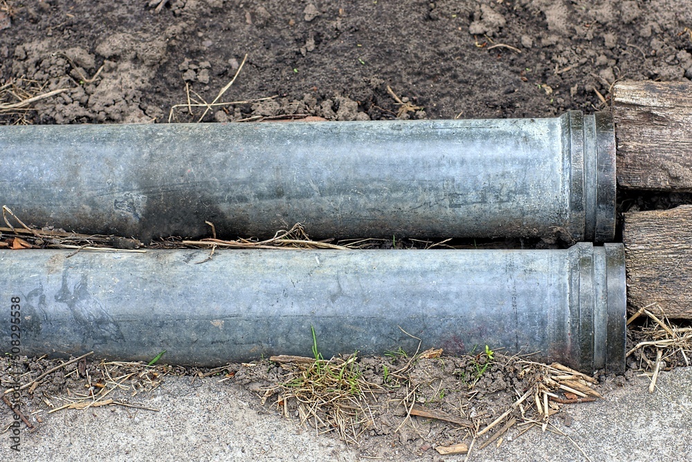 two gray black plastic pipes lie on brown ground in the street two gray black plastic pipes lie on brown ground in the street