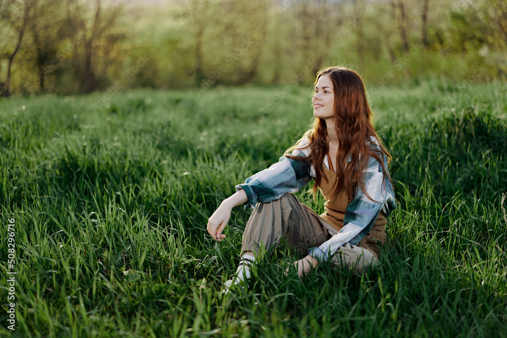 A young beautiful woman sits on the green grass in the park and looks out into the setting sun A young beautiful woman sits on the green grass in the park and looks out into the setting sun