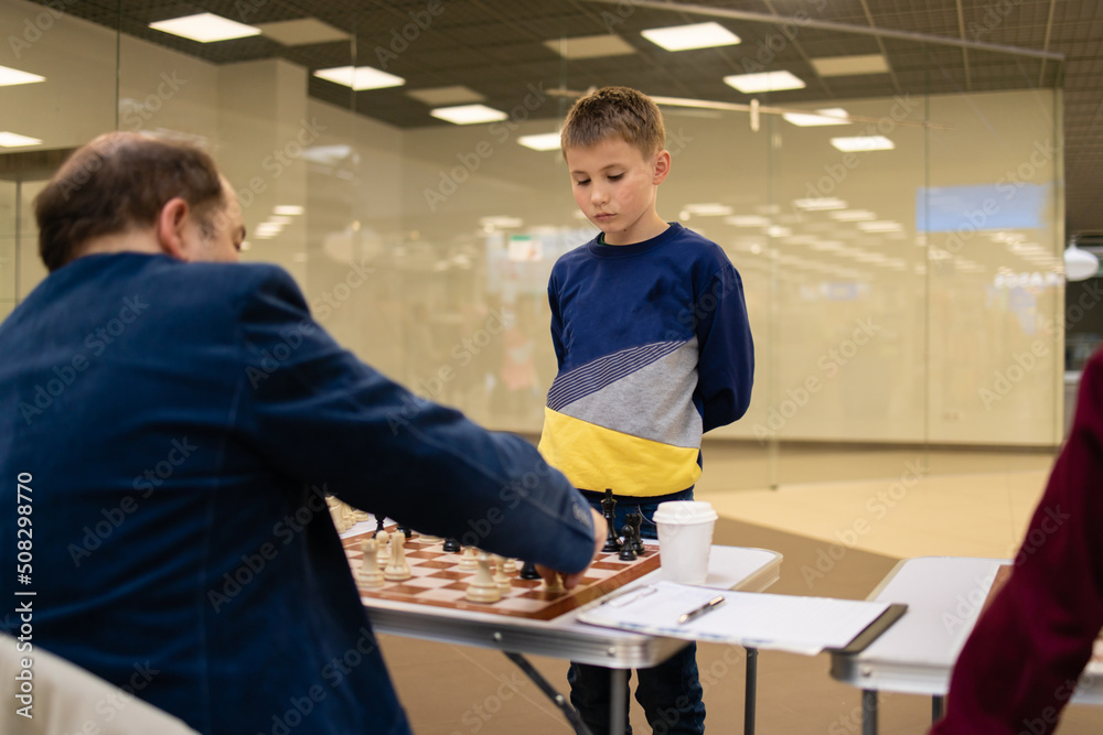 Obraz premium Concentrated boy develops a chess strategy, plays a board game with adult professor .Chess game in action. Board in details. 