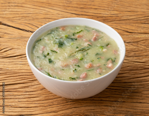 Traditional portuguese green soup with potato, green cabbage and sausage in a bowl over wooden table