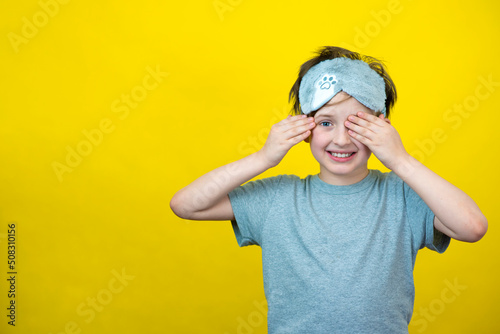 A smiling little boy in a fashionable accessory sleep mask. yellow background