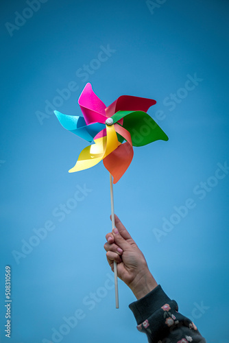 Hand of a girl holding a pinwheel with the colors of the rainbow on the background of the sky