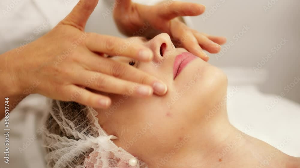 Beautician cosmetologist makes face massage and applies a moisturizer cream, professional  cosmetic procedure in a beauty clinic salon for client. Skincare and cosmetology spa concept.