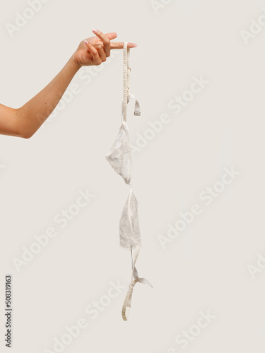 a woman's hand holds a lace bra. light background
