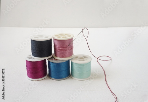 Five Spools of Cotton Sewing Thread in Differnt Colors with Threaded Needle on White Canvas Background photo