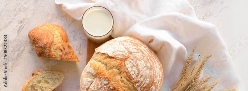 Loaf of bread and glass of fresh milk on light background, top view