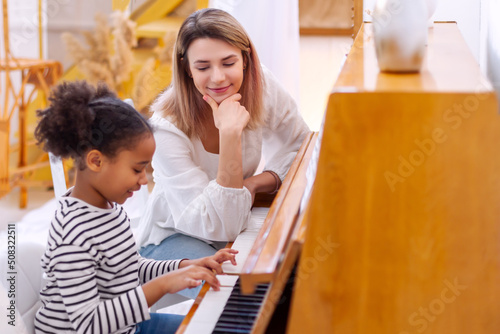 Woman and girl playing a piano. Beautiful mom teaching her daughter playing a piano. The piano teacher experienced pianist gives classes to a young little student. Hobby and activity for the children.