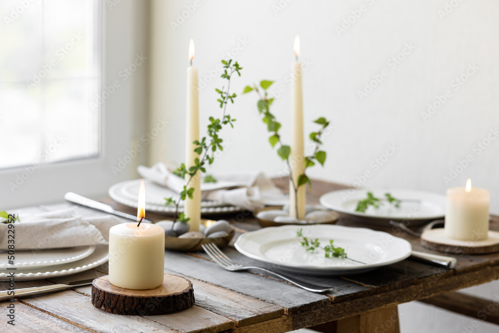 Rustic zero waste wedding decor with natural elements. Wooden table, candles, linen napkins, branches with green leaves. Eco-friendly decoration for the special dinner. Romantic and cozy place