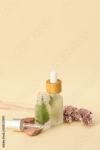 Bottles of natural serum and flowers on beige background