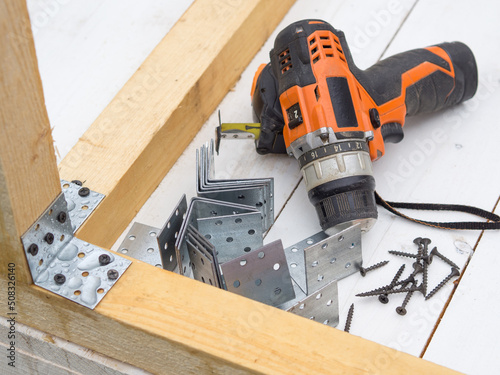 screwdriver, self-tapping screws and metal corners in the workplace, the concept of assembling a wooden house