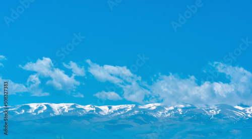 blue mountain sky landscape, snowy peaks of a mountain range in the distance under a clear sky with clouds