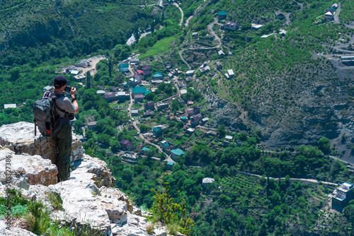 male backpacker takes pictures of a mountain village from a high cliff