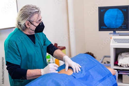 Картината върху платно Doctor practices the infiltration of drugs to the patient in the area affected by the pain, using the ultrasound support to visualize the anatomical components of the spine