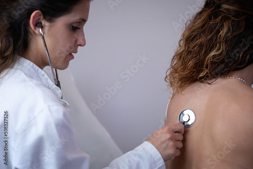 Doctor visits patient in her office. Doctor listens to the patient's chest with a stethoscope, observing the breathing and internal noises of the organism. Traditional medical examination. photo