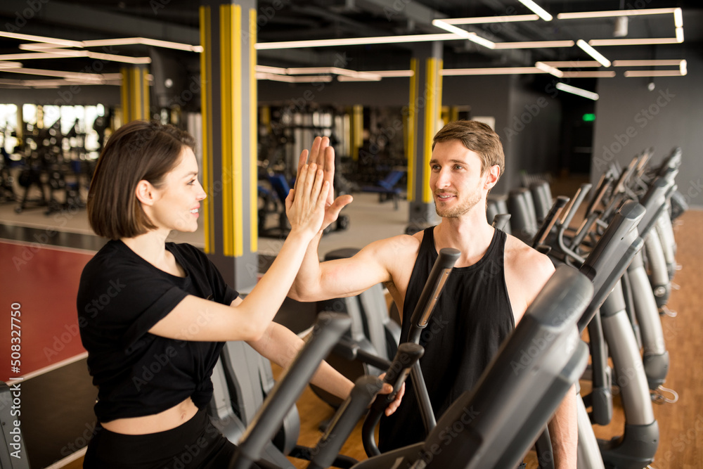 Young fit woman giving a high-five to trainer while she training on elliptical trainer in modern gym Young fit woman giving a high-five to trainer while she training on elliptical trainer in modern gym