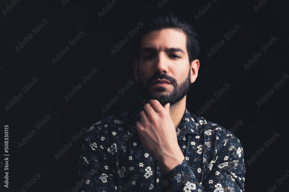 Fototapeta premium bearded Latin American handsome male person touching his chin looking severely into the camera copy space black background studio shot medium closeup. High quality photo