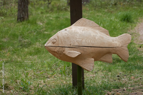 Decorative wooden European perch fish in a forest park. Handmade, traditional craft, landscaping design themes photo