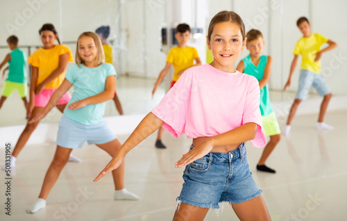 Happy tween girl dancing with children during group class in modern choreographic studio.