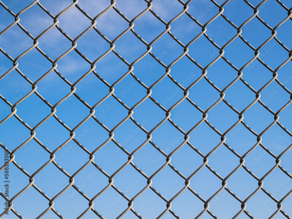 Fence with metal grid in perspective. Metal fence Part of a metal grid fence in blue sky at the background Fence with metal grid in perspective. Metal fence Part of a metal grid fence in blue sky at the background