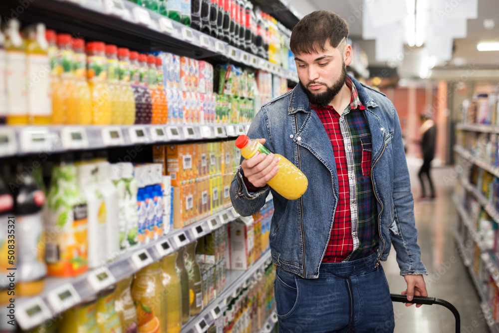 Portrait of focused young man purchasing sweet soft drinks in food shop