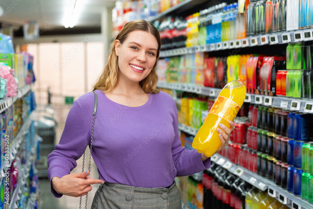 Portrait of young happy glad positive smiling woman satisfied with choosed carbonated soft drinks in food store
