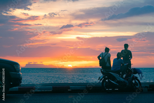 Three young women with a scooter standing on the road by the sea and enjoy the colorful sunset