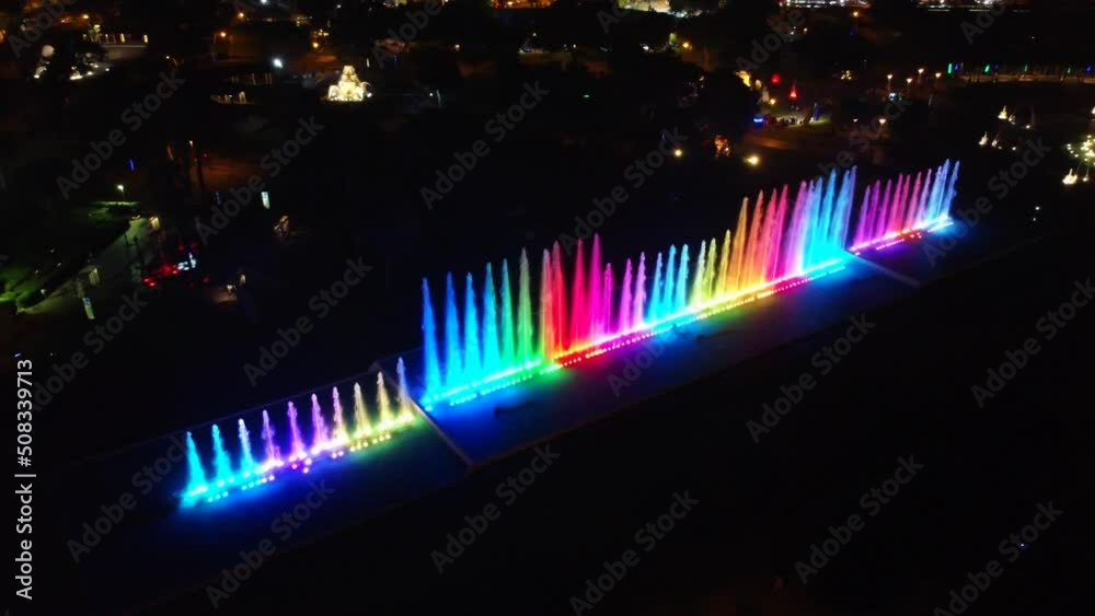 Nighttime drone video of water park with laser lights in fountains, creating a colorful water show. Shot slowly turning with camera slightly tilted down. Lima, Peru.