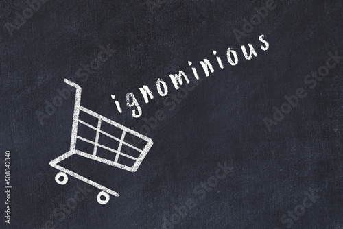 Chalk drawing of shopping cart and word ignominious on black chalboard. Concept of globalization and mass consuming photo