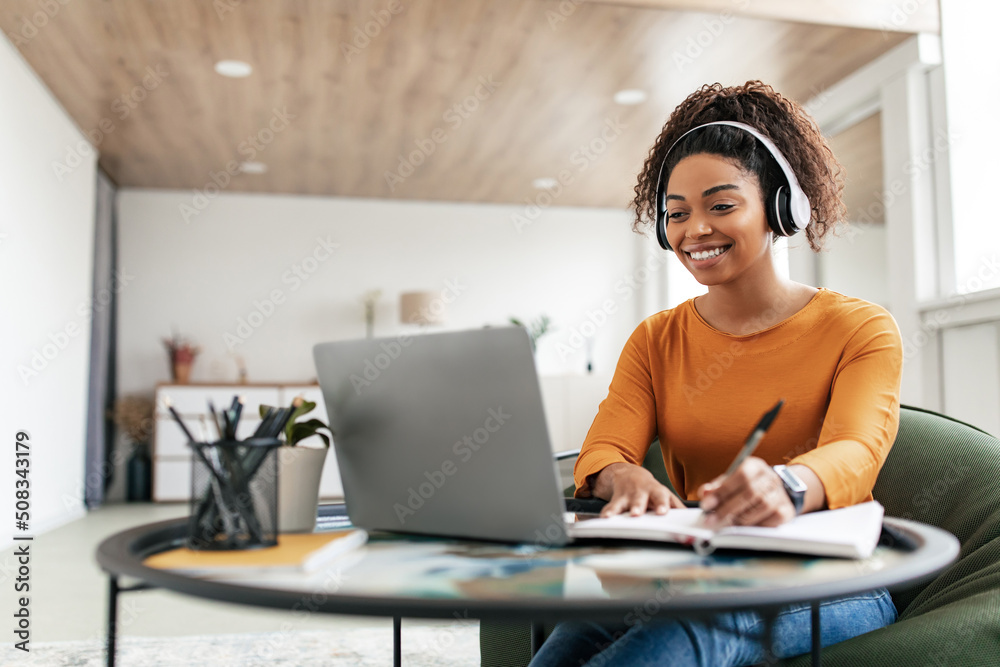 Woman sitting at desk, using computer and writing in notebook