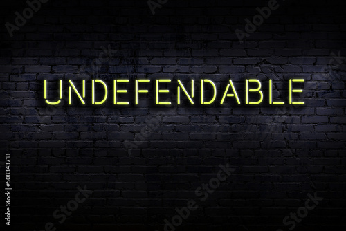 Night view of neon sign on brick wall with inscription undefendable photo