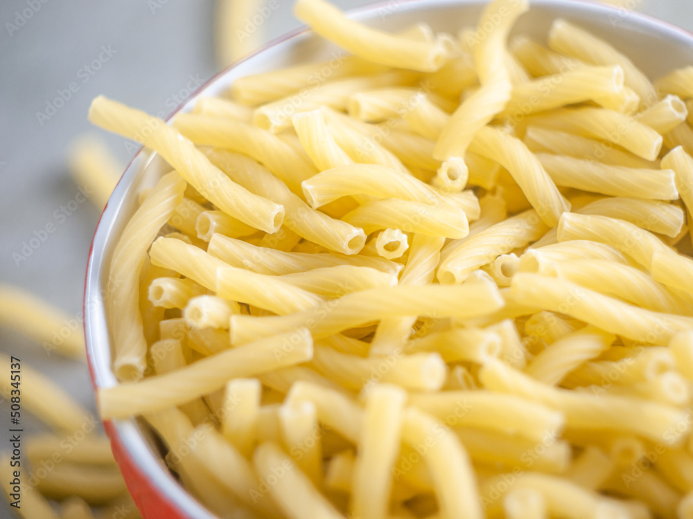 Closeup of Italian food yellow raw uncooked vermicelli, macaroni, noodle, pastry, pasta on the isolated red bowl (close-up,meal, cuisine, cooking, gray, dry, dish, studio, plate,dinner, tile, cement) Closeup of Italian food yellow raw uncooked vermicelli, macaroni, noodle, pastry, pasta on the isolated red bowl (close-up,meal, cuisine, cooking, gray, dry, dish, studio, plate,dinner, tile, cement)