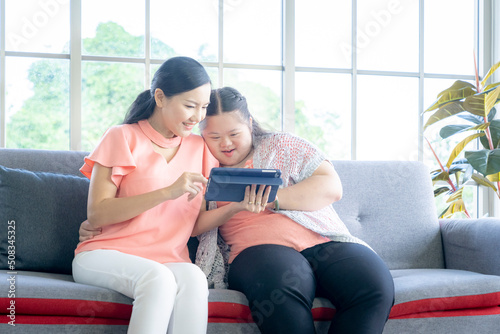 Asian person with Down syndrome using computer with her mom and having fun together at living room