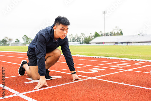 Young handsome chinese man doing star pose before running exercise on track in sport stadium. Challenge race of athletes running in the starting point