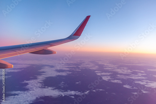 Airplane flight at sunset or dawn. Aircraft's wing and land seen through the illuminator. View from the window of the plane. Airplane, Aircraft. Traveling by air. 